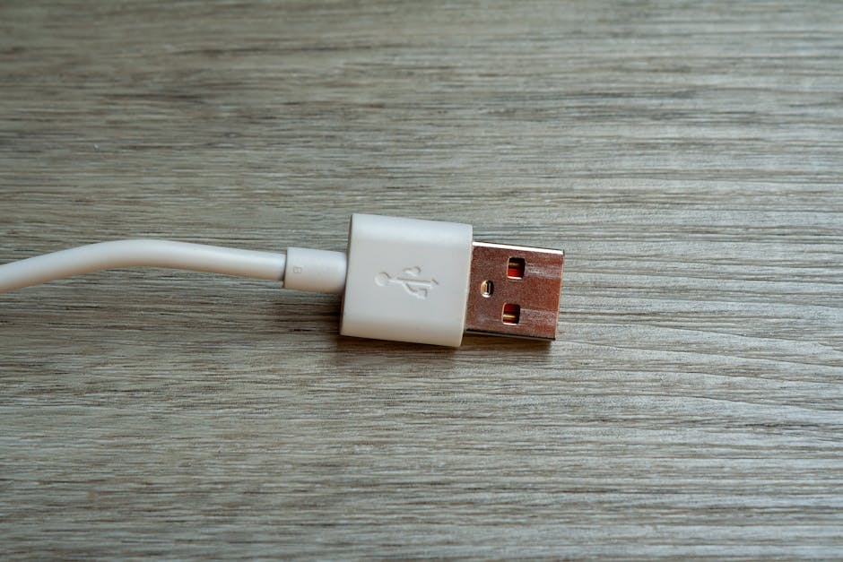 A close-up of a white USB cable connector resting on a wooden surface, illustrating the everyday charging chain.