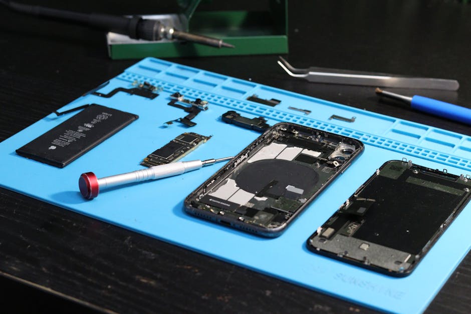 Disassembled smartphone parts laid out on a blue repair mat, showing the layered display assembly.