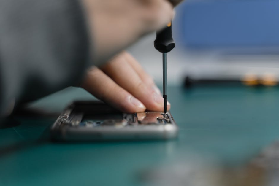 A close-up of a hand fixing an electronic device with a screwdriver.
