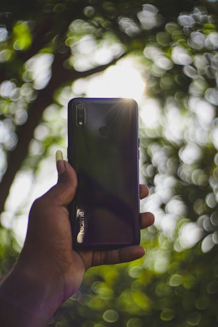 A close-up of a smartphone held in a hand with sunlight and a soft bokeh background.