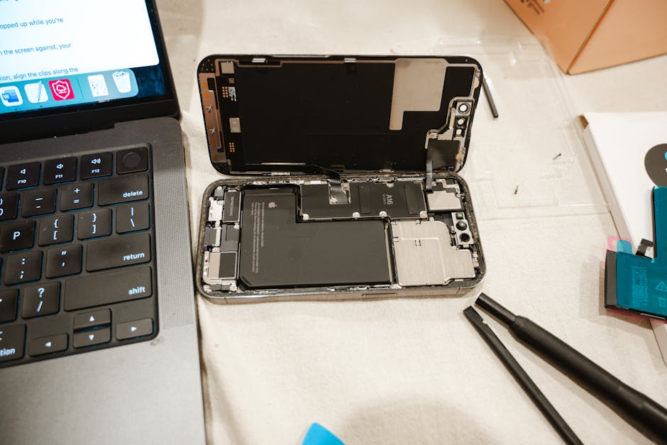 An open iPhone with repair tools and a laptop, showing a battery replacement in progress.